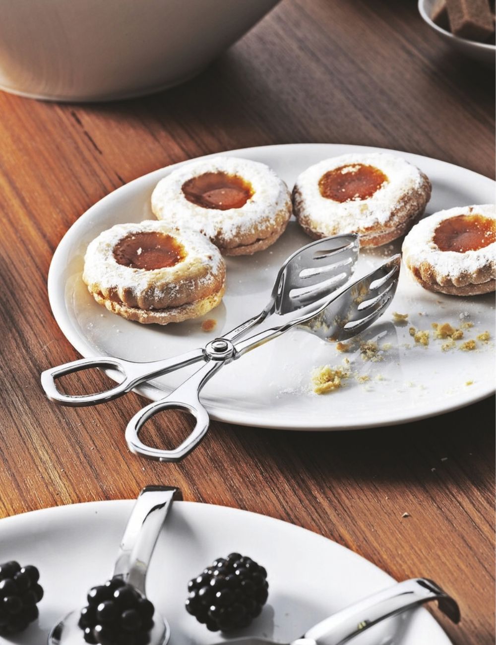 PADERNO Living stainless steel pastry tongs on a plate of jam-filled biscuits dusted with icing sugar